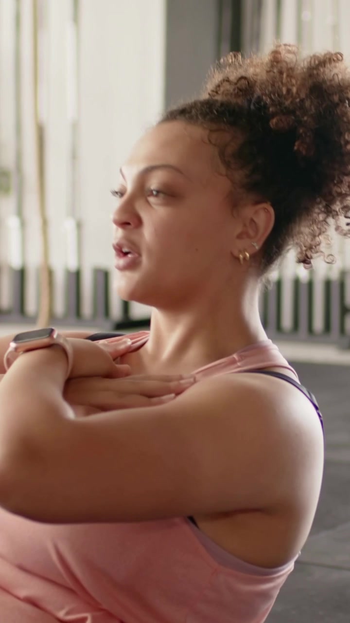 Video vertical: Mujer de rosa yendo a la colchoneta y haciendo abdominales para el core en el gimnasio, gráficos guiando la postura.