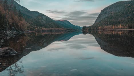 Forest-covered-mountains,-passing-dark-clouds,-and-rocky-shores-reflected-in-the-still-waters-of-the-shallow-lake