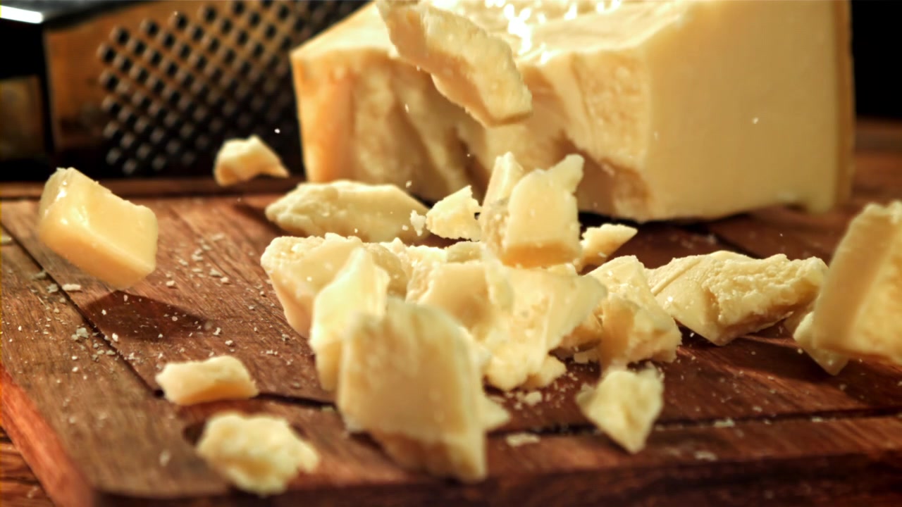 Délicieux morceaux de fromage parmesan tombant sur une planche en bois rustique.