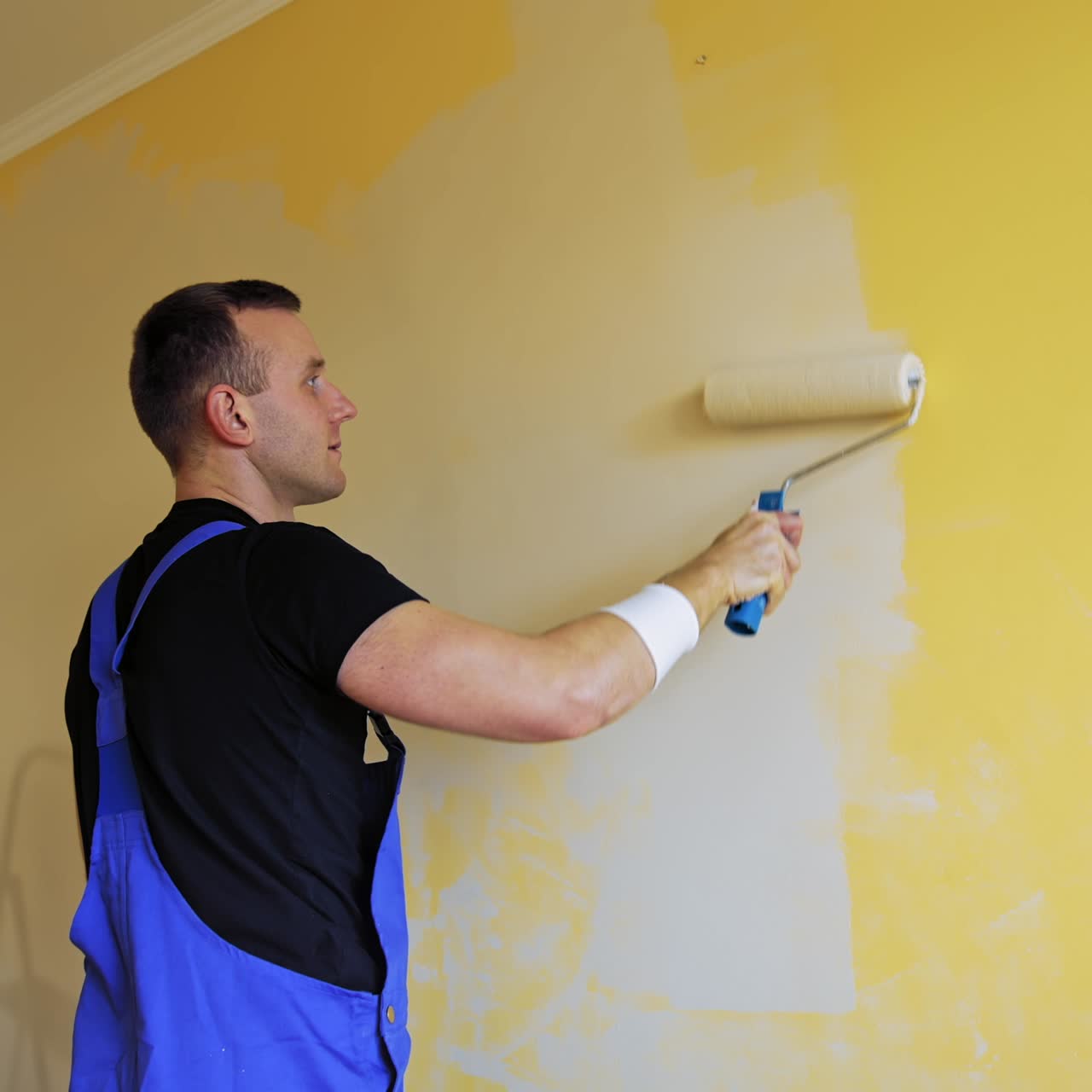 Man with roller painting wall. Young professional male painting wall in new home