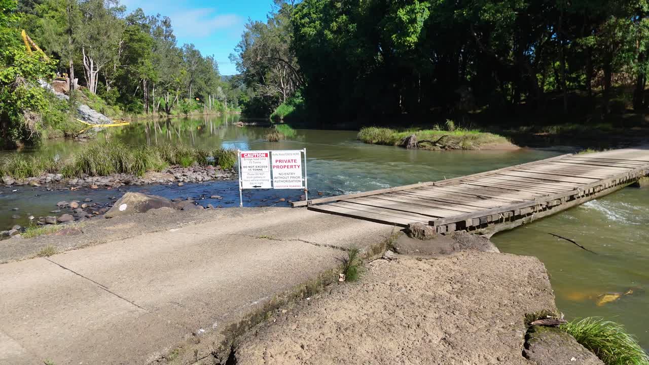 Aerial view of a wooden bridge over Tweed Creek, surrounded by lush greenery under bright daylight