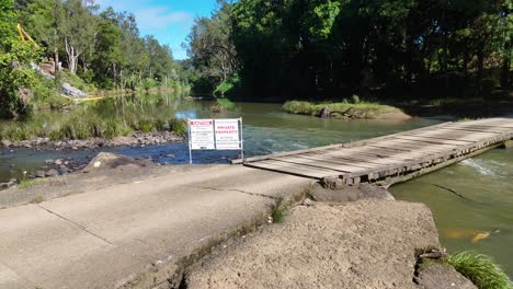 aerial view of a wooden bridge over tweed creek, surrounded by lush greenery under bright daylight