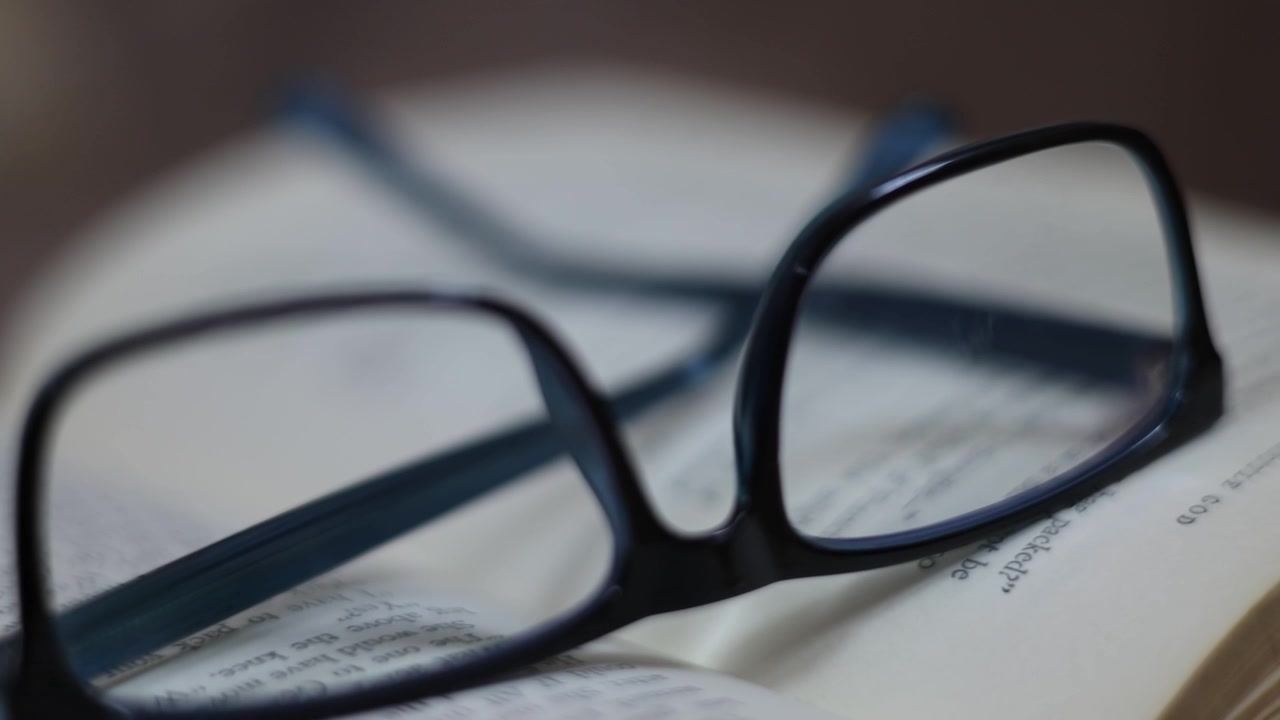 Gafas apoyadas en un libro antiguo abierto, simbolizando la esencia del conocimiento, toma macro