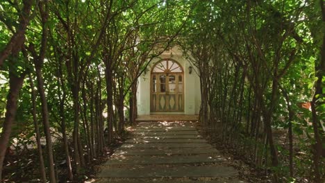 Tunnel-Trees-Walking-Towards-a-Wooden-Arched-Doorway-Building