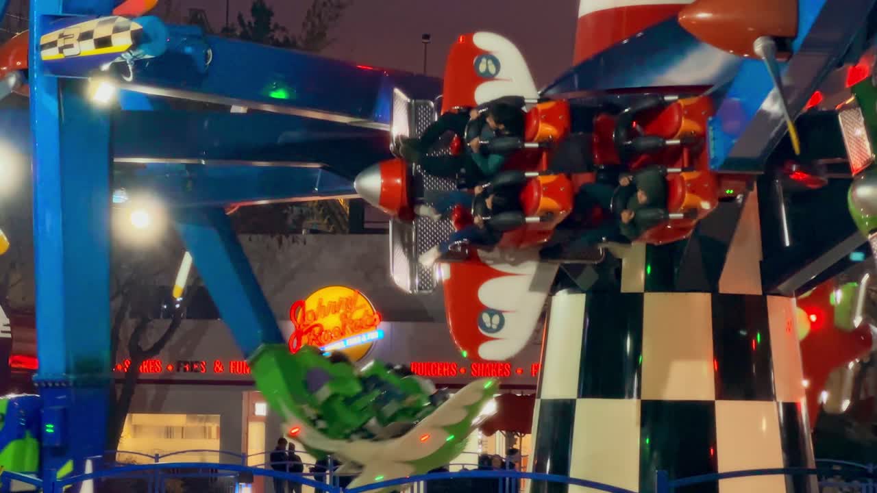 Airplanes down at Fantasilandia amusement park, Johnny Rockets sign at night, Santiago, Chile.