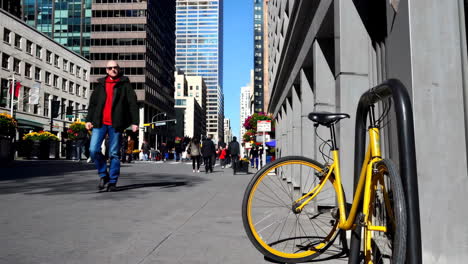 yellow bicycle parked on a sunny city street with pedestrians and skyscrapers