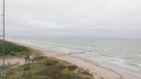 estableciendo una vista aérea de la costa del mar báltico en un día nublado, un viejo muelle de madera, una playa de arena blanca, grandes olas de tormenta aplastando la costa, cambios climáticos, un amplio tiro de drones avanzando alto