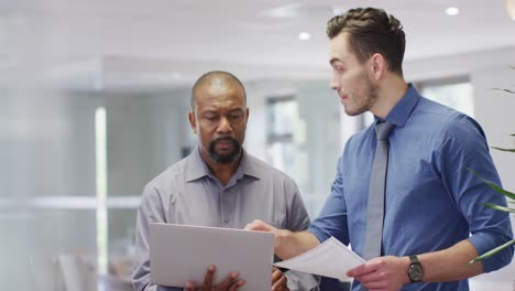 group of diverse business people using laptop and talking in office, slow motion