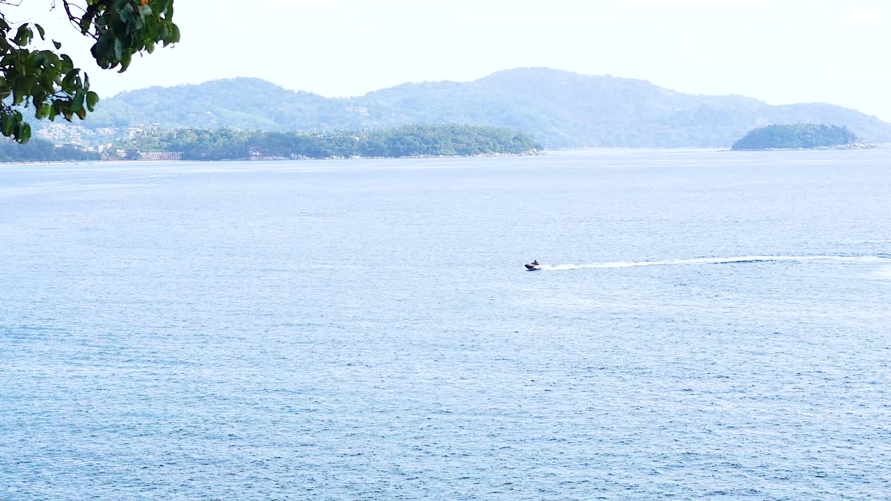 A jet ski speeds across the calm blue sea near Phuket, Thailand, under bright daylight with distant islands in view