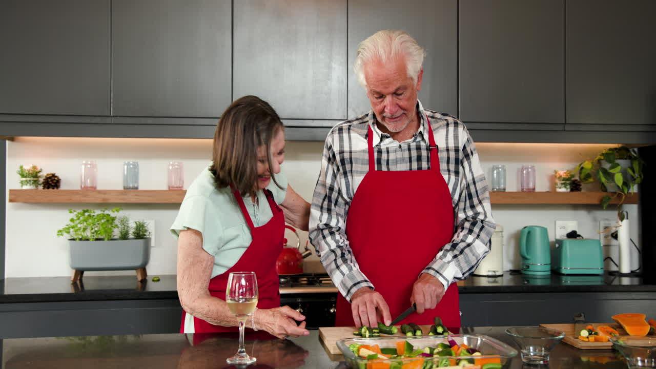 Chopping vegetables in kitchen, senior couple wearing red aprons, cooking together, at home