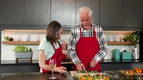 chopping vegetables in kitchen, senior couple wearing red aprons, cooking together, at home