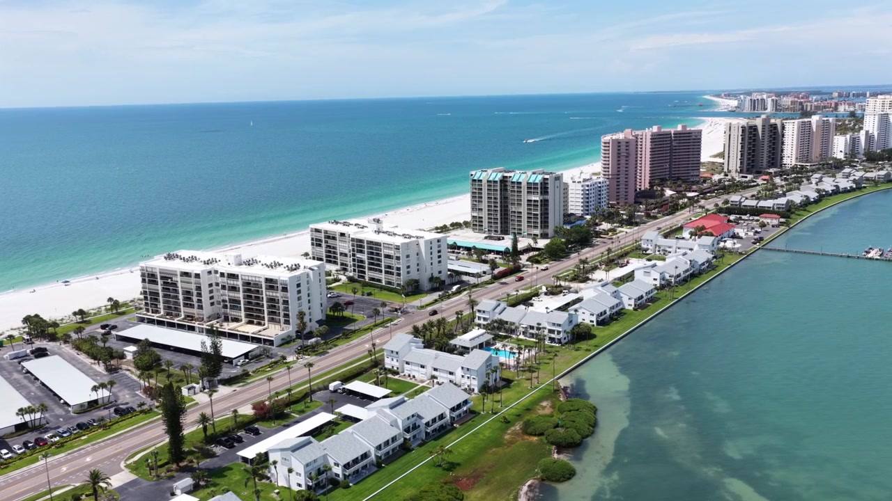 Condomini a molti piani costeggiano l'isola di Clearwater Beach, le onde turchesi del Golfo incontrano la sabbia bianca, la via navigabile intracoastale e le mangrovie delimitano la costa interna. Clearwater Beach, Florida, USA. Ripresa aerea con drone in sorvolo