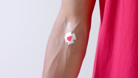primer plano del brazo de un hombre biracial con un corazón pegando yeso en el brazo, sobre un fondo blanco, cámara lenta