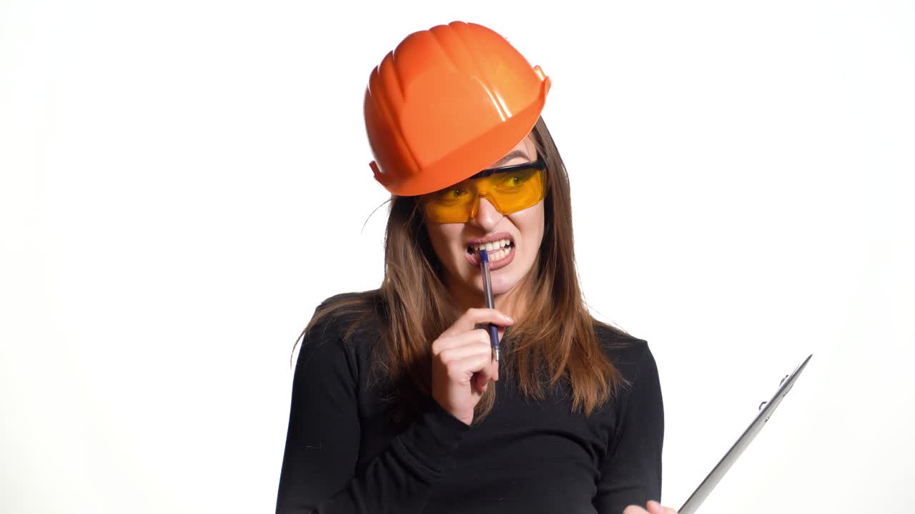 Pretty woman engineer in an orange helmet tells a story about something and holds a folder-tablet with pen in her hands on a white background.