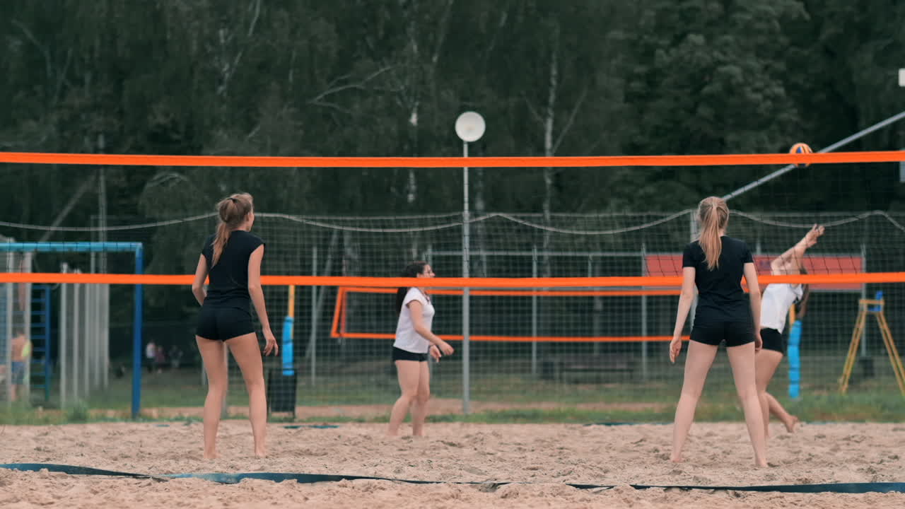 해변에서 볼리볼을 치는 젊은 여성은 공을 때리는 공격을 수행합니다. 느린 모션의 소녀는 공을 때리고 망을 통해 공격을합니다.