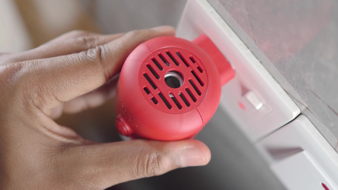 Persona Enchufando un Repelente Eléctrico de Mosquitos Rojo en un Enchufe de Pared
