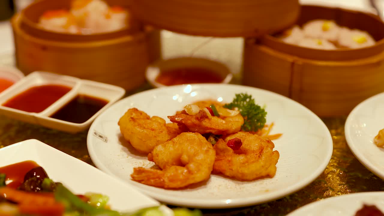 A variety of dim sum dishes, including shrimp and vegetables, arranged on a table in warm lighting