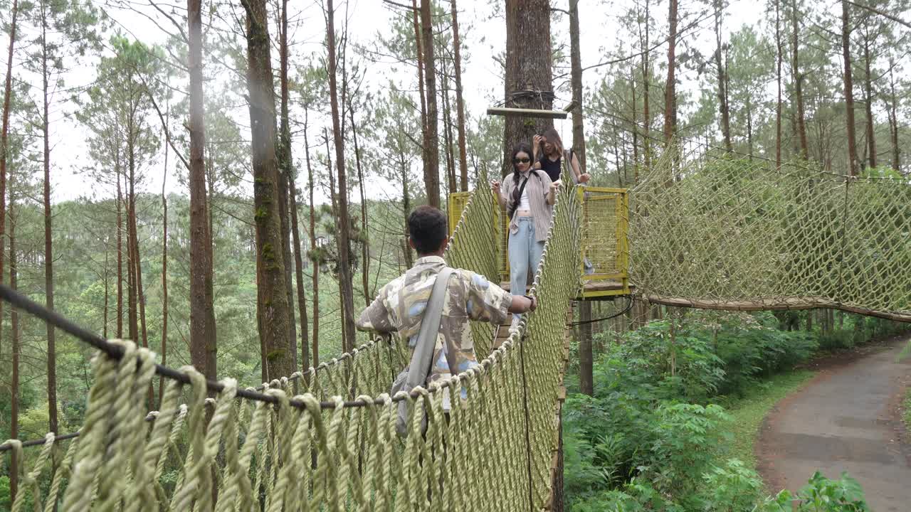 Young Asian Friends Crossing Rope Bridge in Forest Adventure