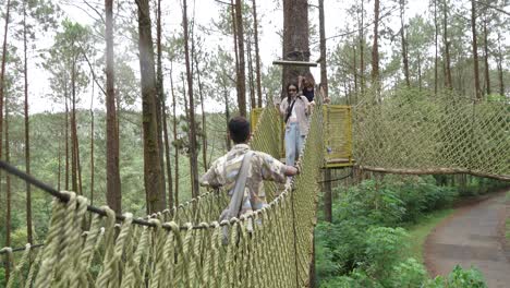 young asian friends crossing rope bridge in forest adventure