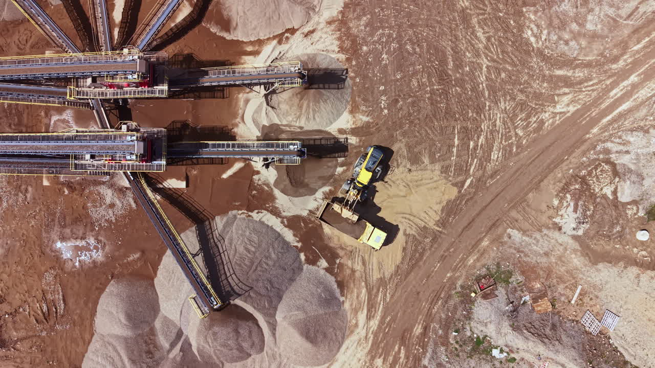 Heavy machinery moves and processes materials at a construction site in the early afternoon sun during a busy workday