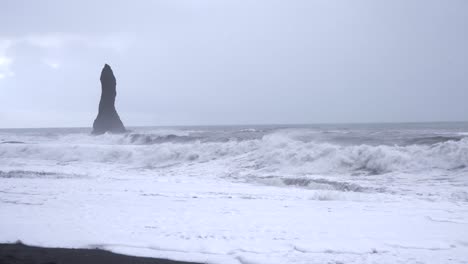 Rock-column-on-Reynisfjara-black-sand-beach-above-sea-waves,-Iceland