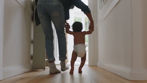 baby taking first steps learning to walk with mother and father teaching toddler at home enjoying parenthood