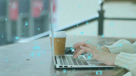 animation of network of digital icons spinning over mid section of a woman using a laptop at a cafe