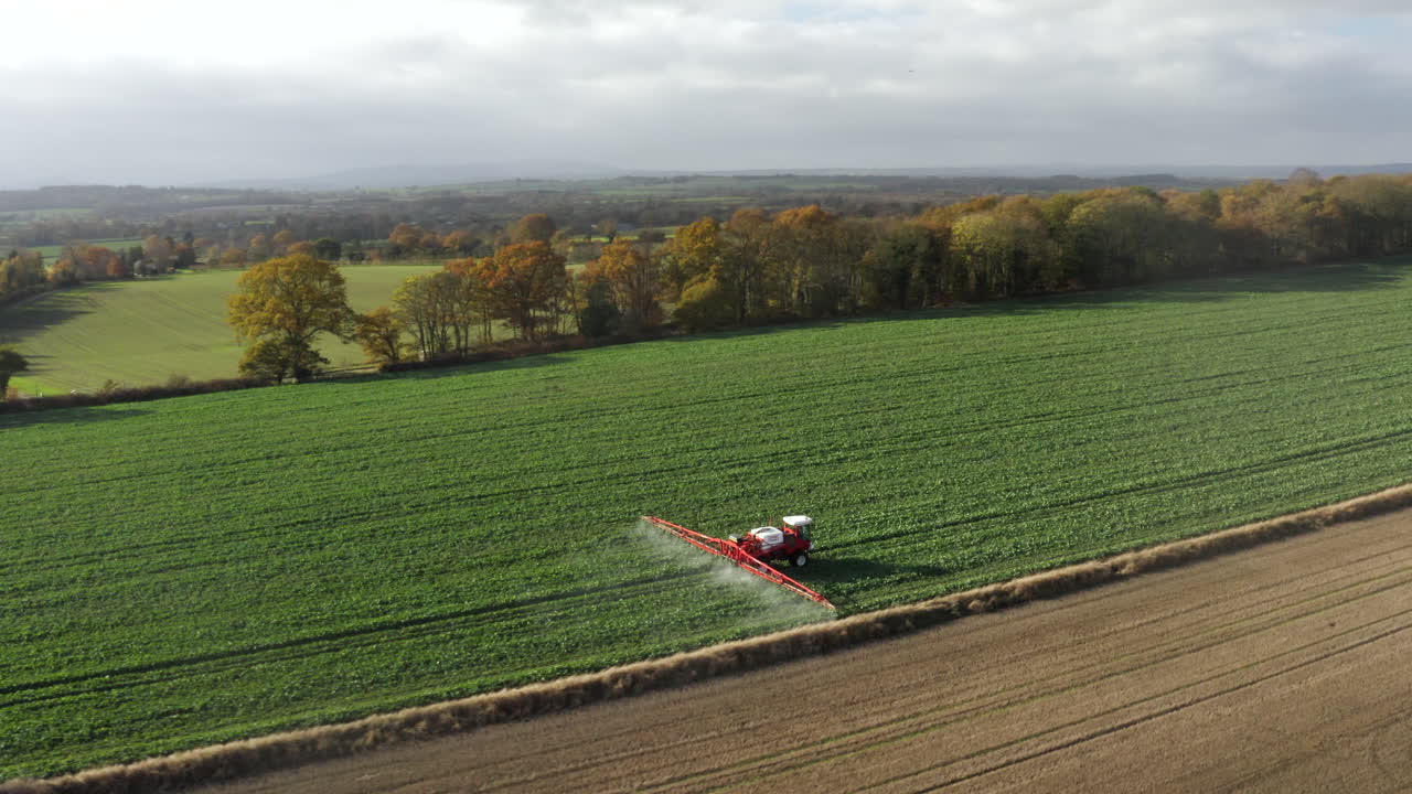 Ripresa aerea circolare di un trattore agricolo che irrora un campo con irroratore, erbicidi e pesticidi in una fattoria rurale