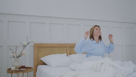 hermosa morena despertando lentamente por la mañana se estira y se levanta de la cama el sol brilla sobre ella desde la gran ventana. feliz joven saluda el nuevo día
