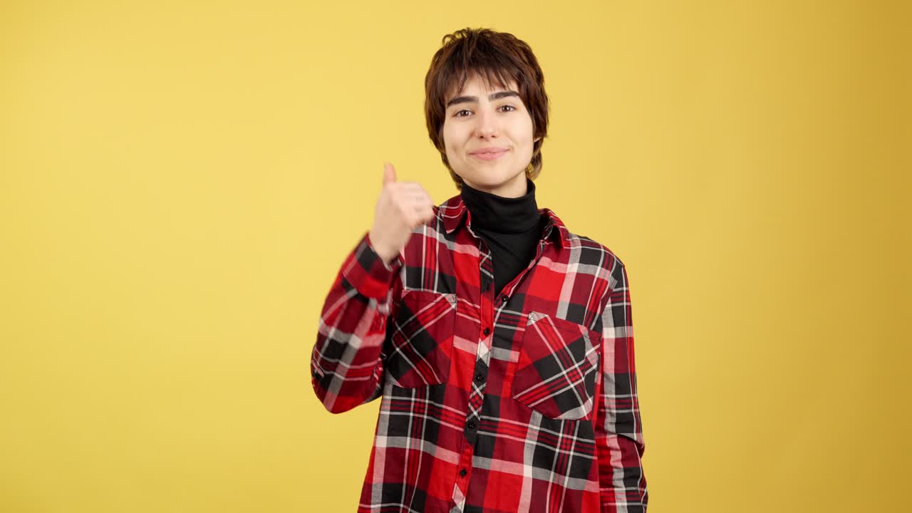 Young woman with short hair giving a thumbs up on a yellow background