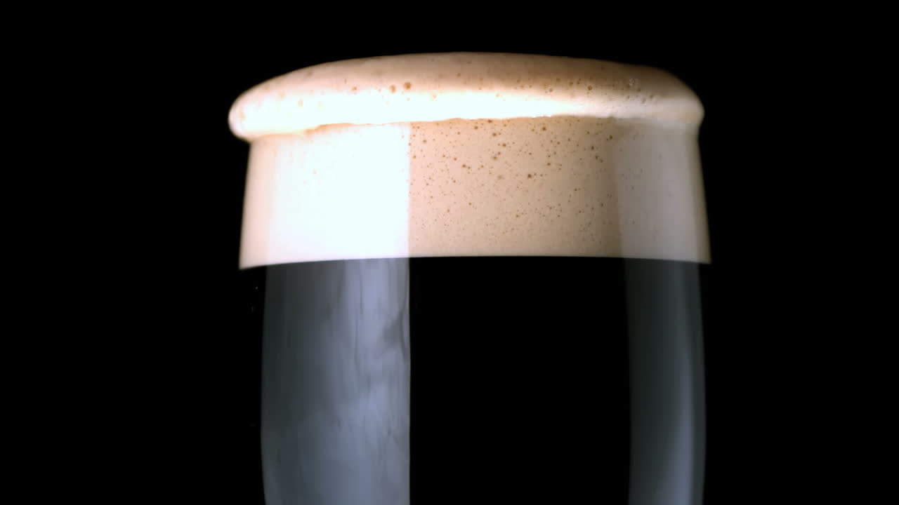 cabeza de espuma asentándose en una pinta de stout sobre un fondo negro