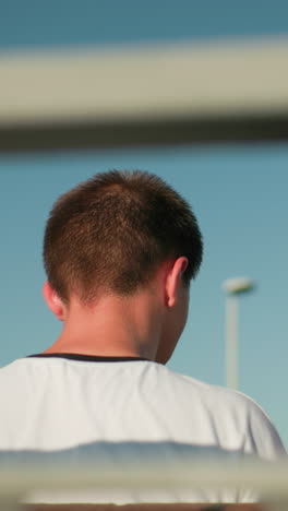 back view of lady with glasses on her head interacting with a man seated close on a bench, against a backdrop of iron railing, light pole, and bright sky