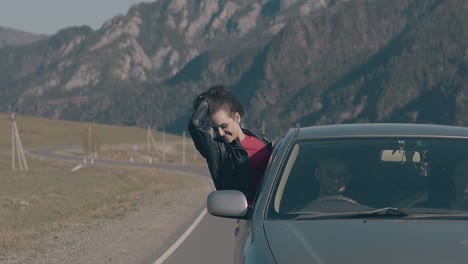 cheerful brunette in leather jacket sits on car window