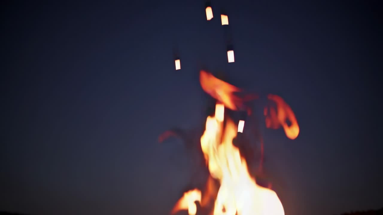 Bonfire burning brightly in the darkness, emitting sparks that fly upwards against the backdrop of a serene night sky, creating a captivating scene of warmth and tranquility