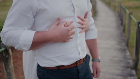 close-up of a couple standing on a boardwalk, with the woman's hands on the man's chest