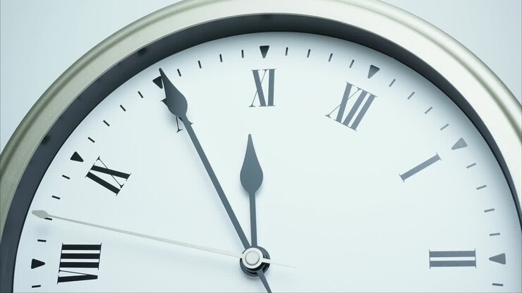 Time lapse silver wall clock short hand points on Roman numerals.