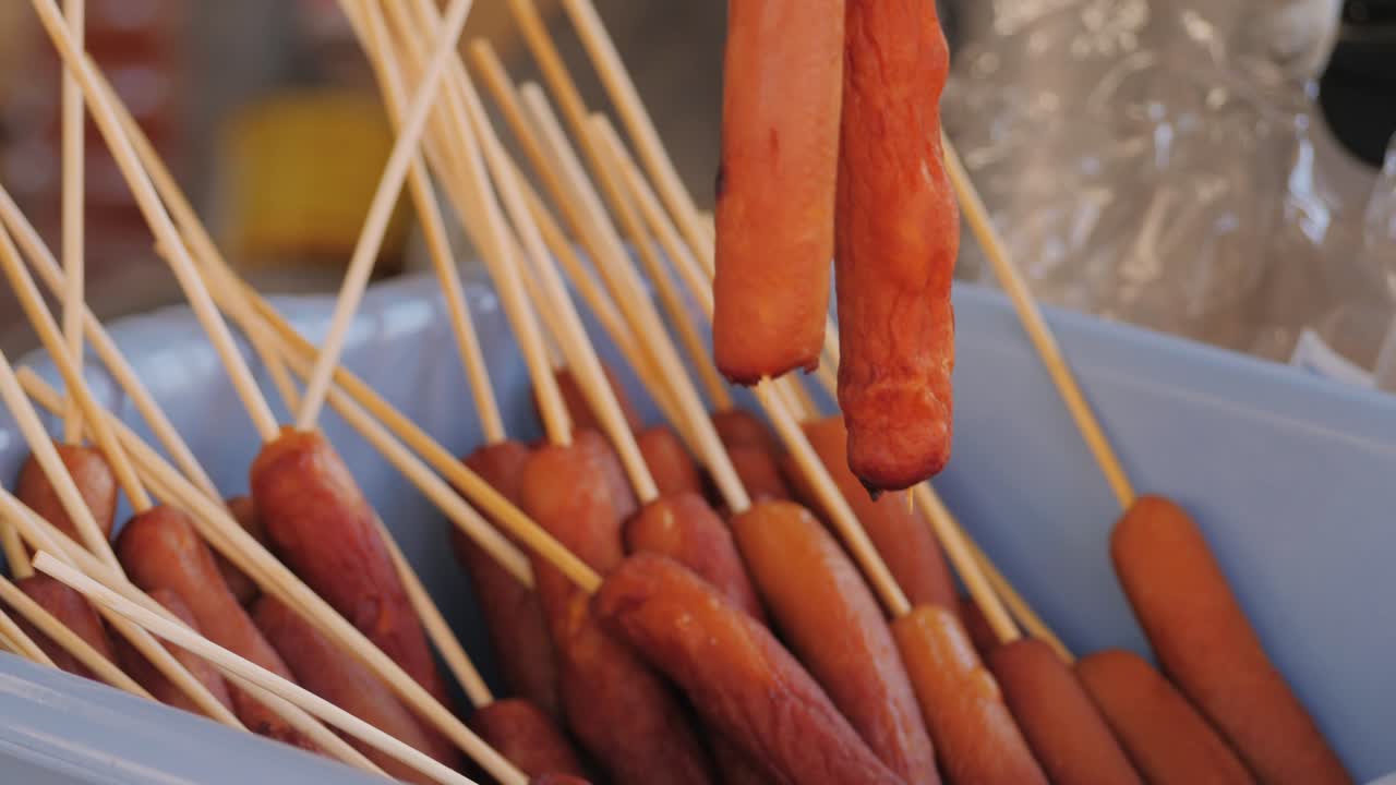 Cooking corn dogs in boiling oil close-up. Traditional asian corndog snacks street food. Fried sausage in breadcrumbs on a stick. Korean Chinese street local market with traditional food. American fast food corndogs with sauce on the top. High quality 4k footage