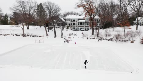 person shoveling snow alone to make outdoor ice hockey skating rink, aerial