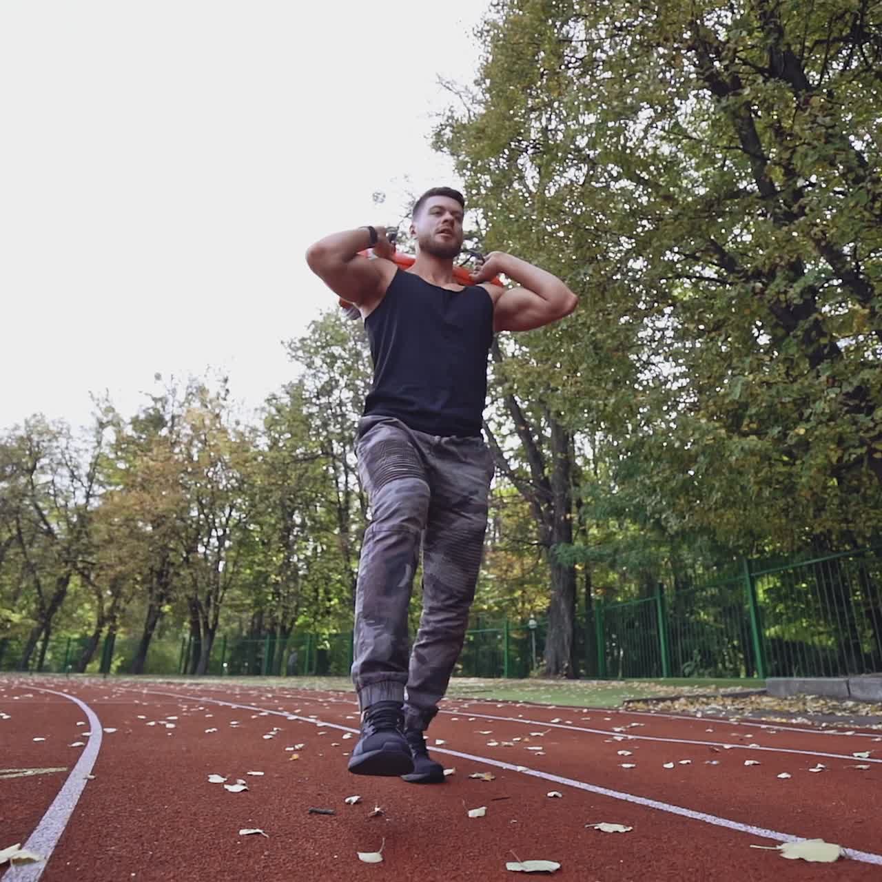 Strong athlete exercising in the stadium. Healthy sportsman doing his workout with heavy weight in the autumn park. Slow motion. View from below.