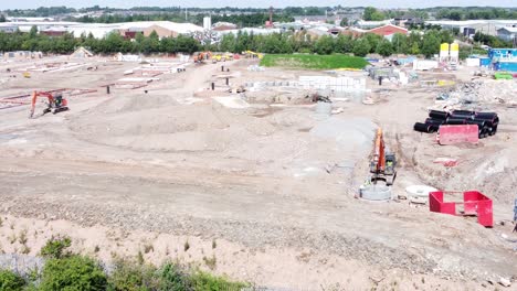 UK-town-housing-development-working-foundation-construction-site-aerial-view-diggers-zoom-out
