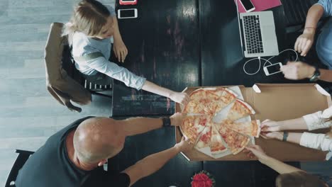 desktop of a creative business team that works on laptops and communicates using smartphones in office. employee brings a box of pizza. coworking. top view
