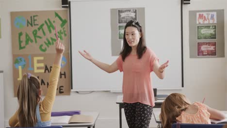 happy diverse female teacher and schoolgirls raising hands in elementary school class, slow motion