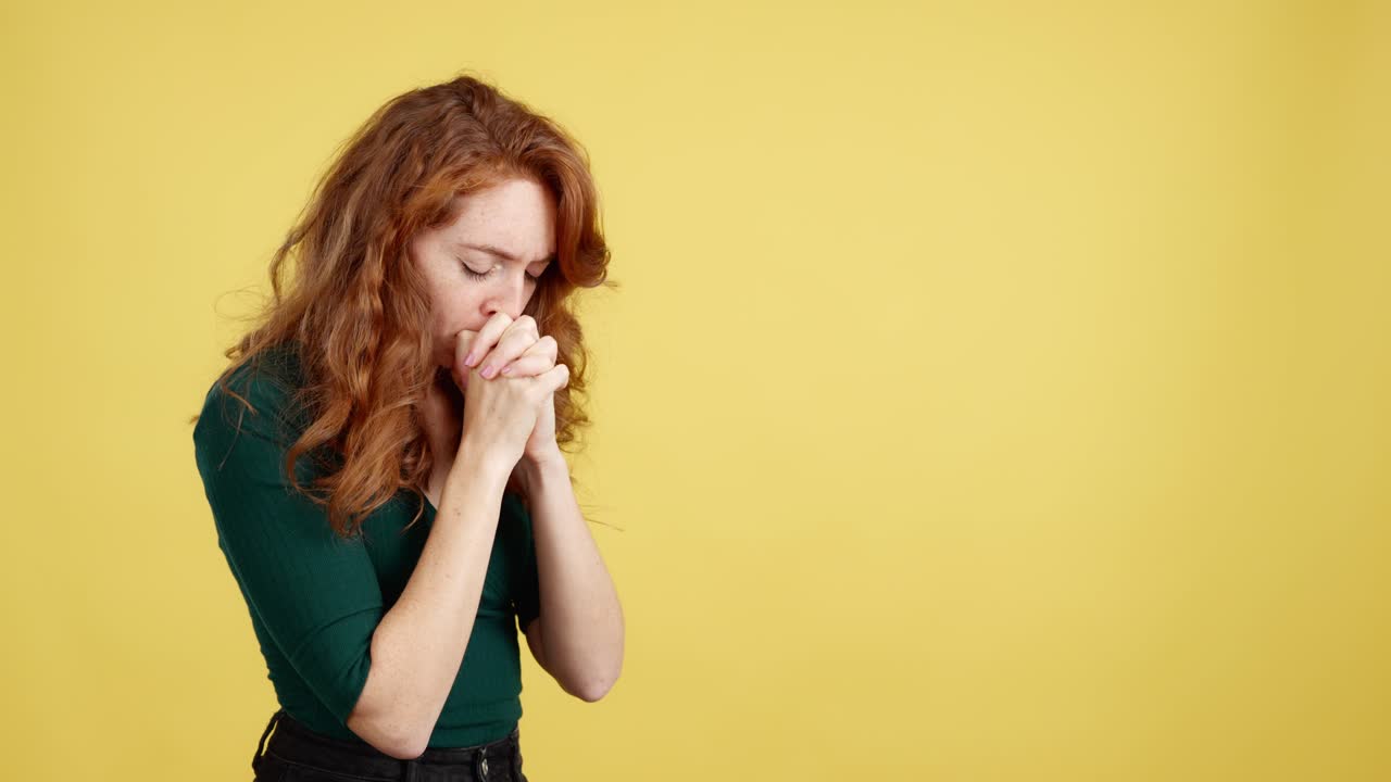 Giovane donna dai capelli rossi immersa nella preghiera o nella contemplazione su sfondo giallo