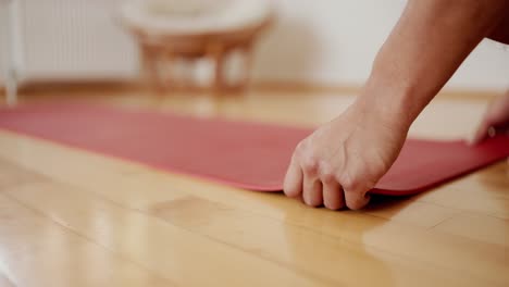 male hands unfolding red yoga mat on wooden floor