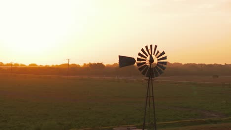 a vintage windmill stands in the foreground in texas at sunrise