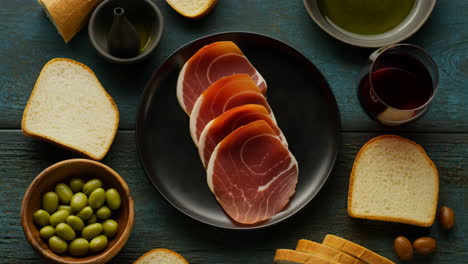 overhead view of prosciutto platter with olives, bread, and red wine