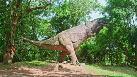 una gran estatua de un dinosaurio, una estatua en un bosque boscoso, una estatura de un dinosauro, la estatua rota