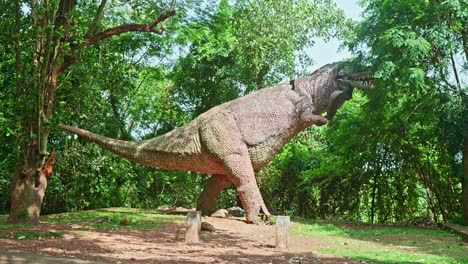 a large statue of a dinosaur ,a statue in a wooded forest ,a statue of a dinosaur , the broken statue