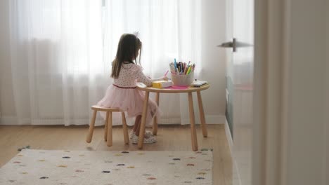 young girl sitting at a table, drawing with colorful crayons. ideal for themes of creativity, childhood development, learning, and art activities in a cozy indoor setting.