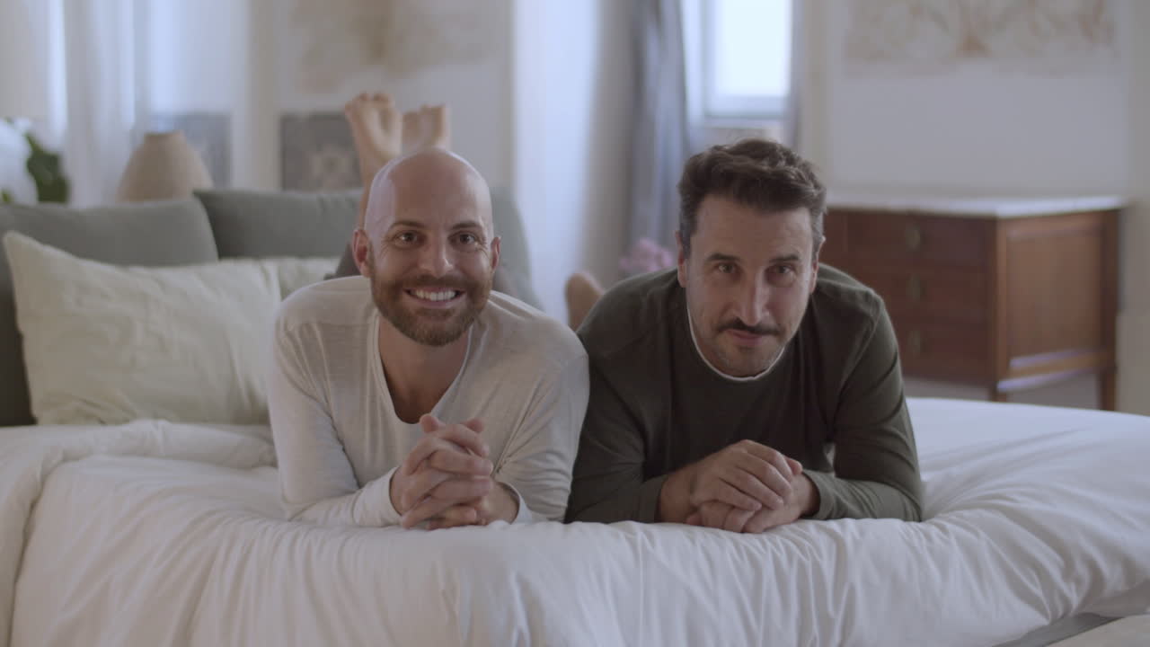 gays felices acostados en la cama por la mañana y mirando a la cámara
